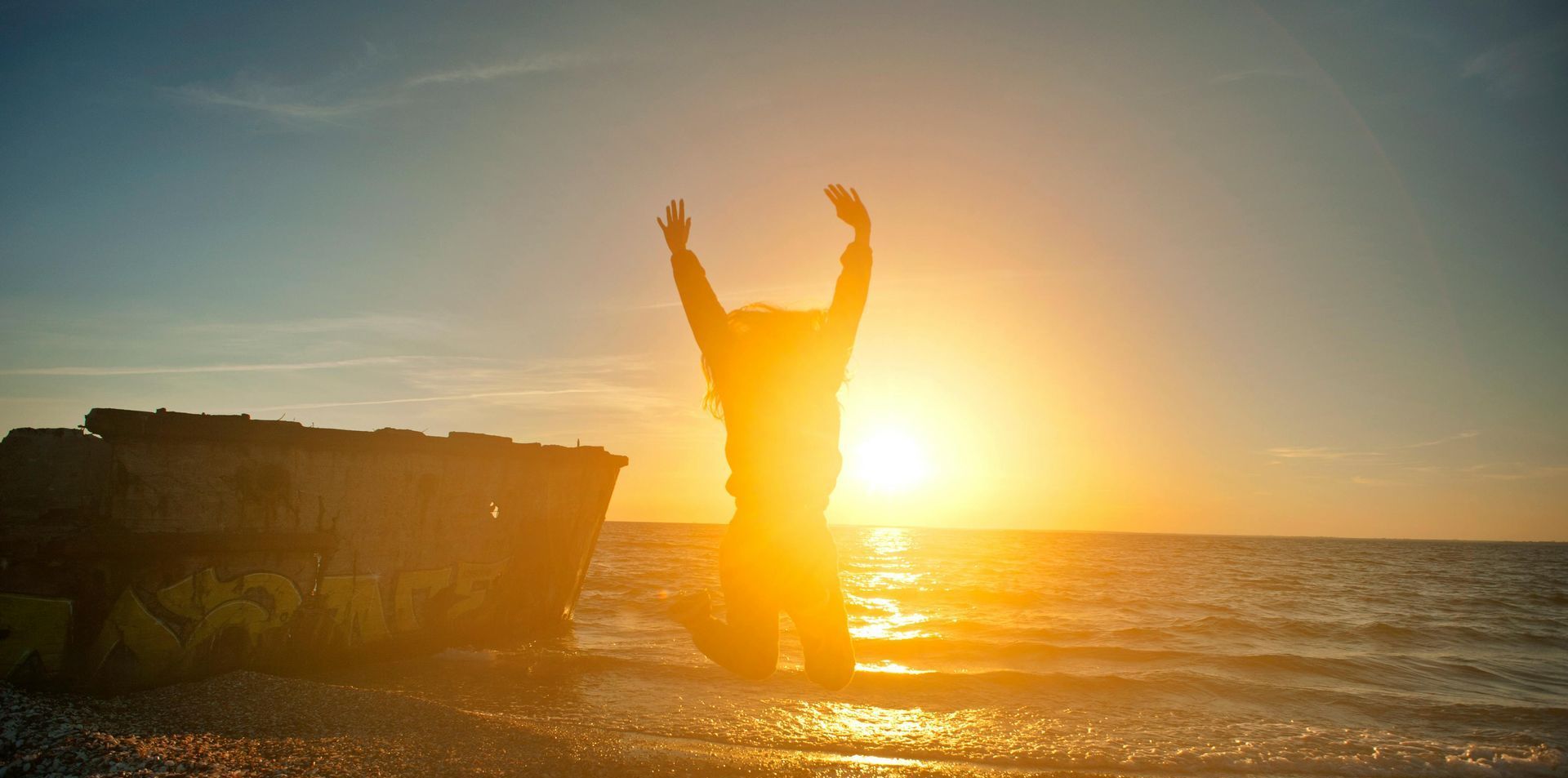 A person is jumping in the air on the beach at sunset.