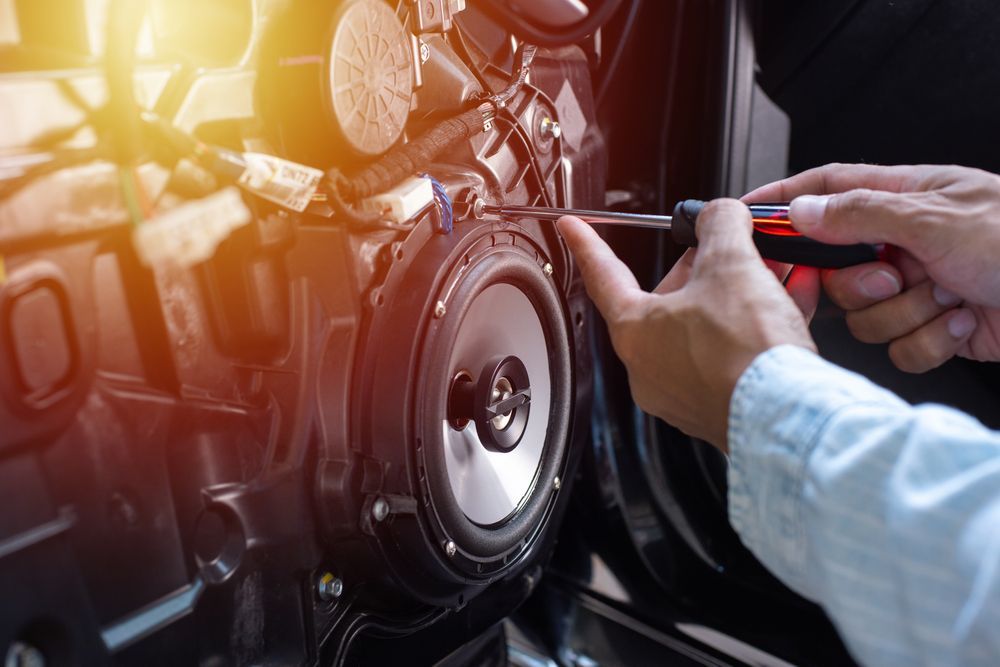 Person Installing Car Speaker With a Screwdriver Inside a Car Door — Mullumbimby Auto Electrical in Mullumbimby, NSW