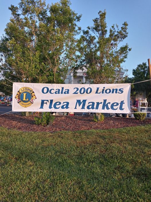 Banner for Ocala 200 Lions Flea Market, with logo, in front of trees and grass.