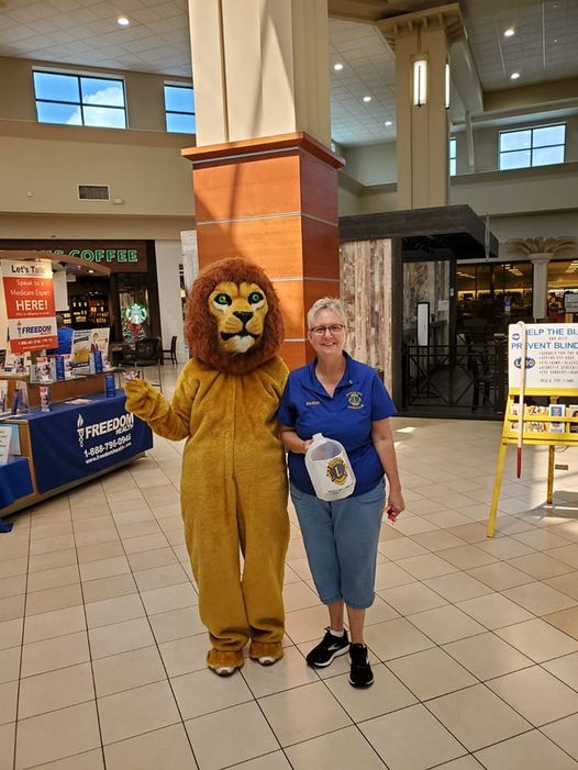 A woman and a lion mascot pose in a mall. The woman holds a donation jug.