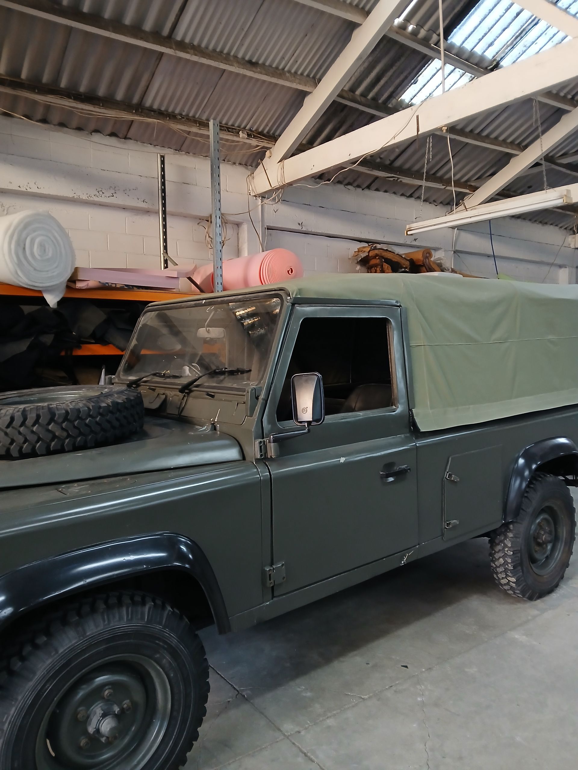 Dark green Land Rover with canvas top parked inside a warehouse.
