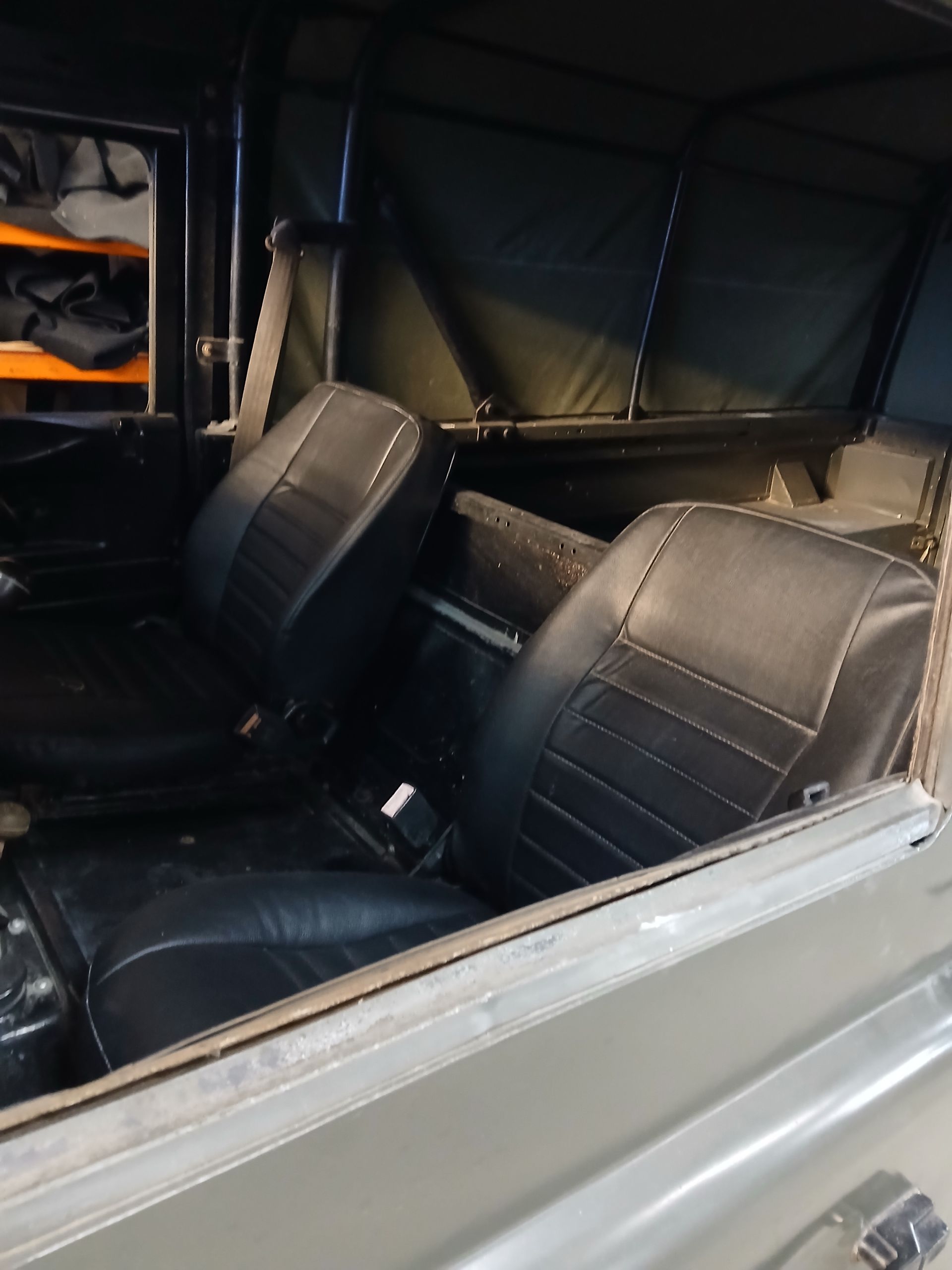 Black leather seats inside an open-top vehicle with a green canvas roof.