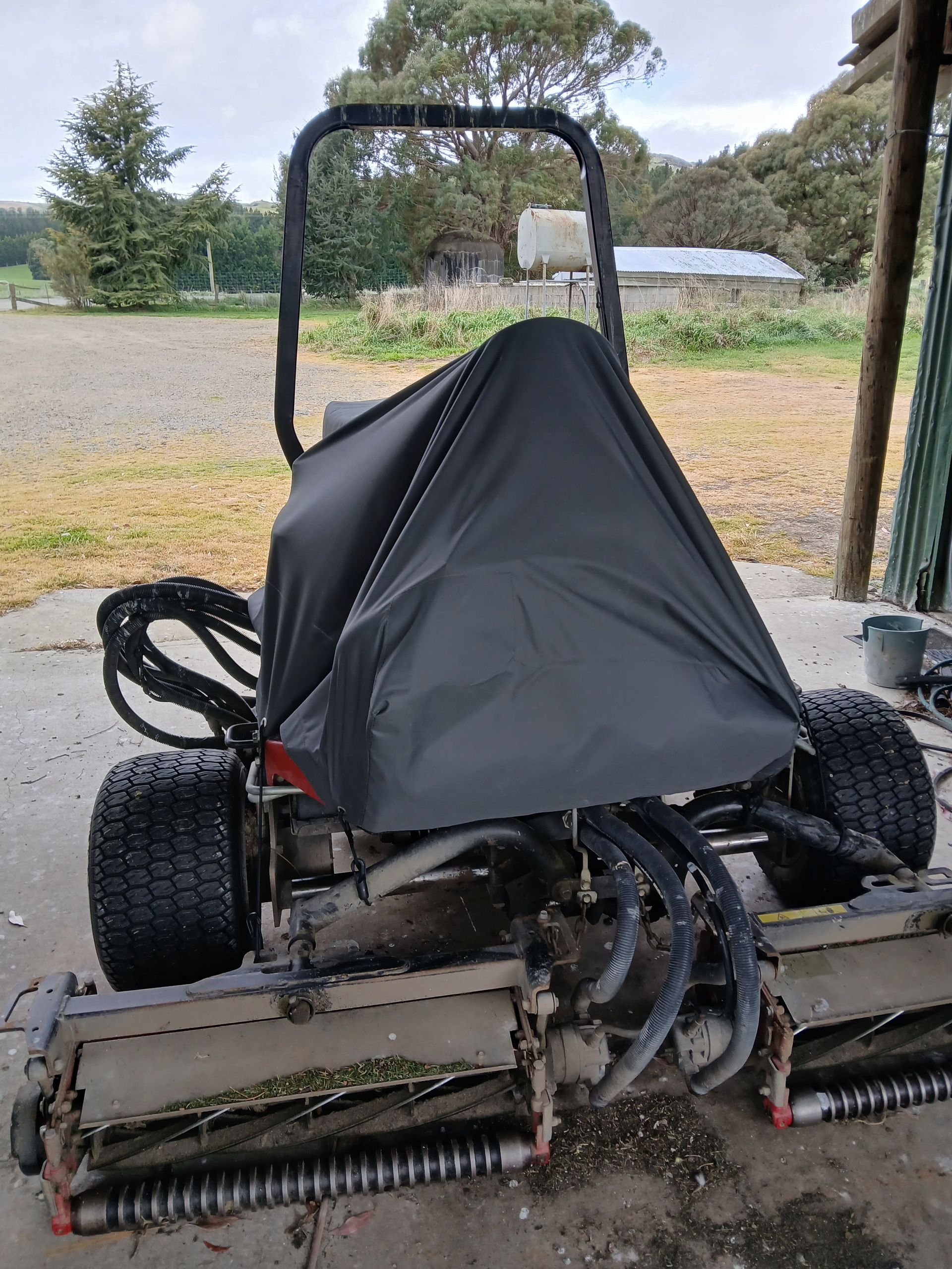 A black covered commercial lawn mower parked on a concrete surface, with a rural background.