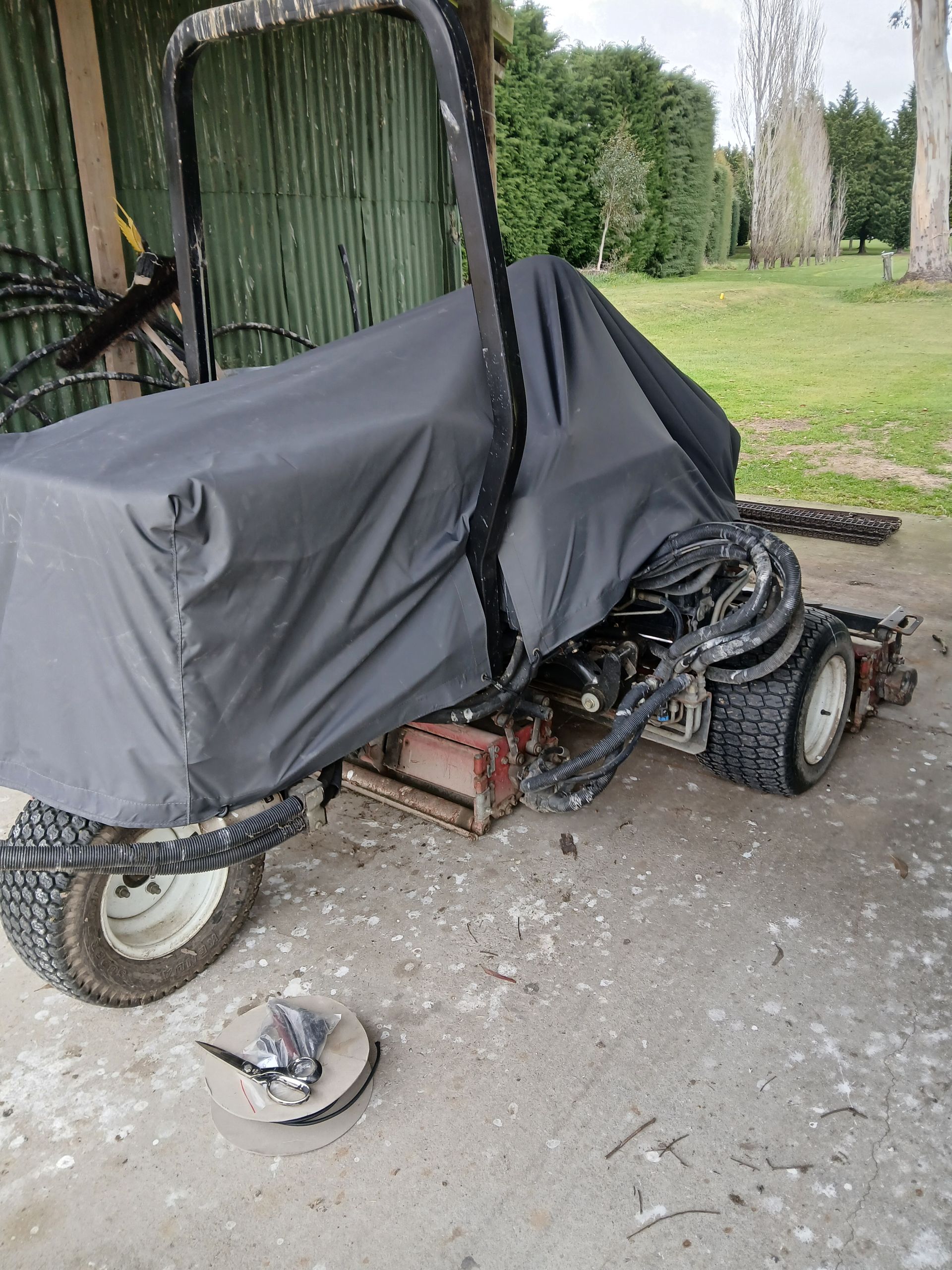 Riding lawnmower covered in black tarp, parked on a concrete surface outdoors.