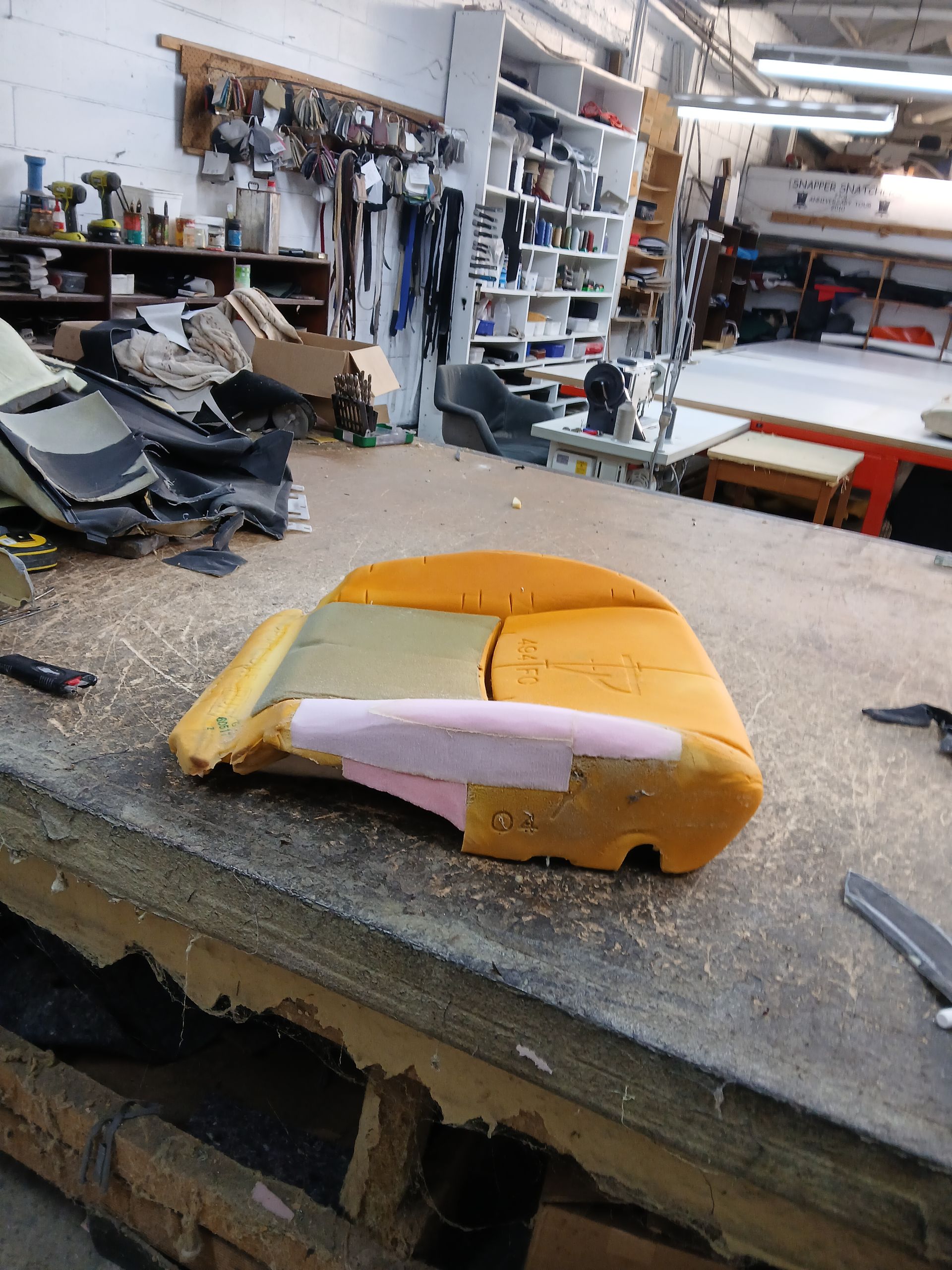 Car seat cushion being repaired in a workshop with tools and materials in the background.