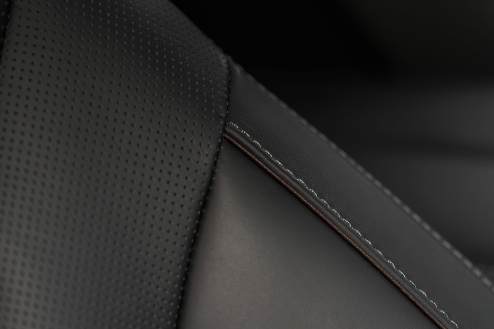 Black leather car seat with white stitching and perforated details.