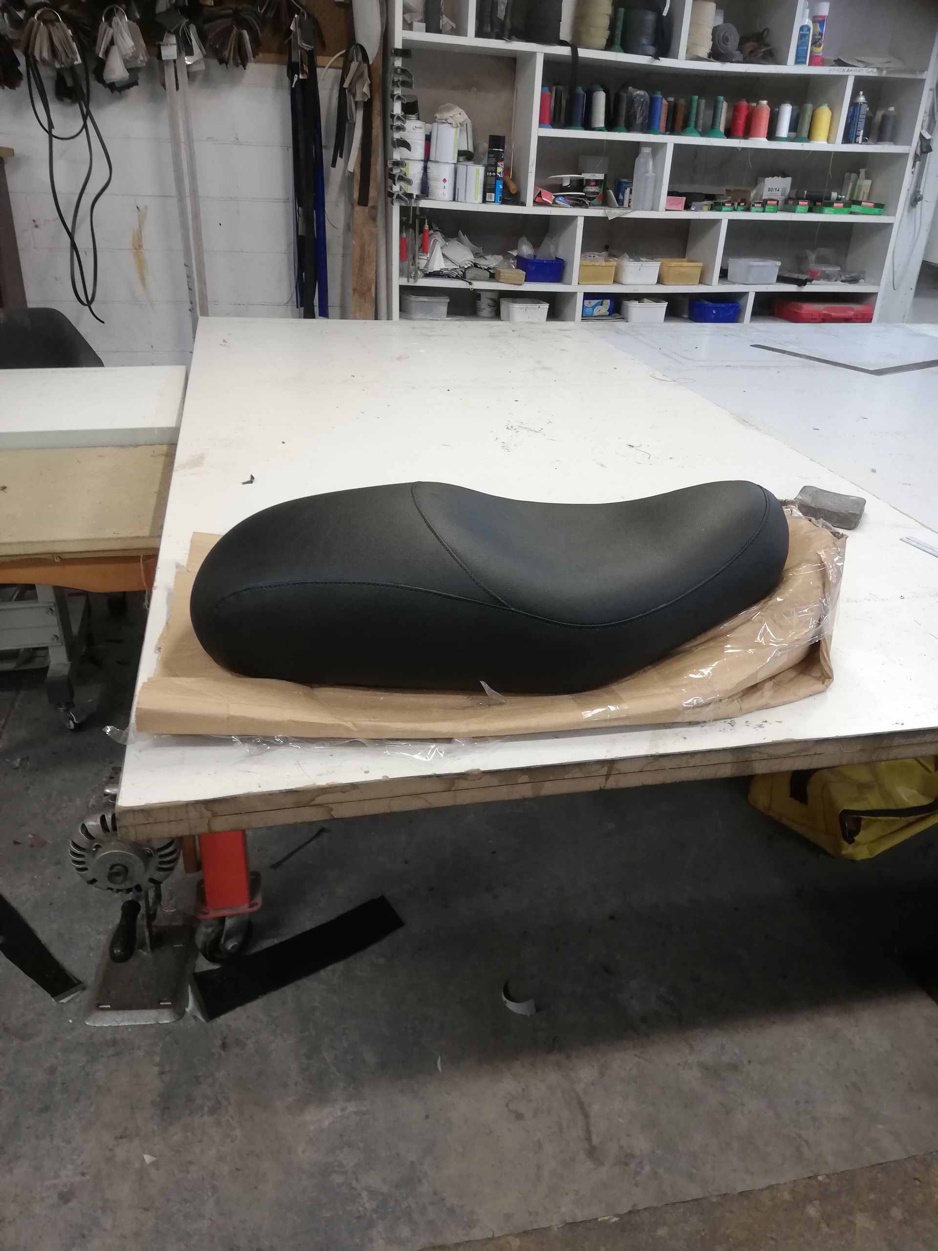 Black motorcycle seat on a white table in a workshop setting.