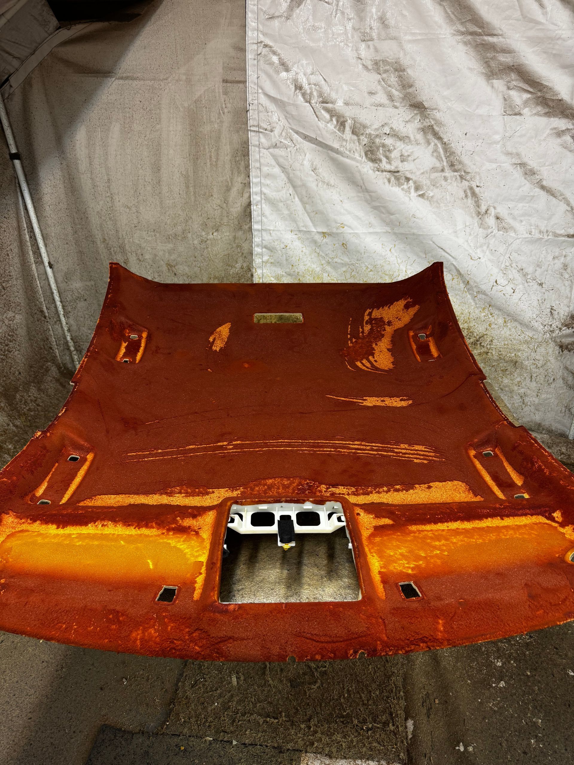 A worn, orange-brown car headliner with holes and detached fabric, laid out on a light-colored surface.