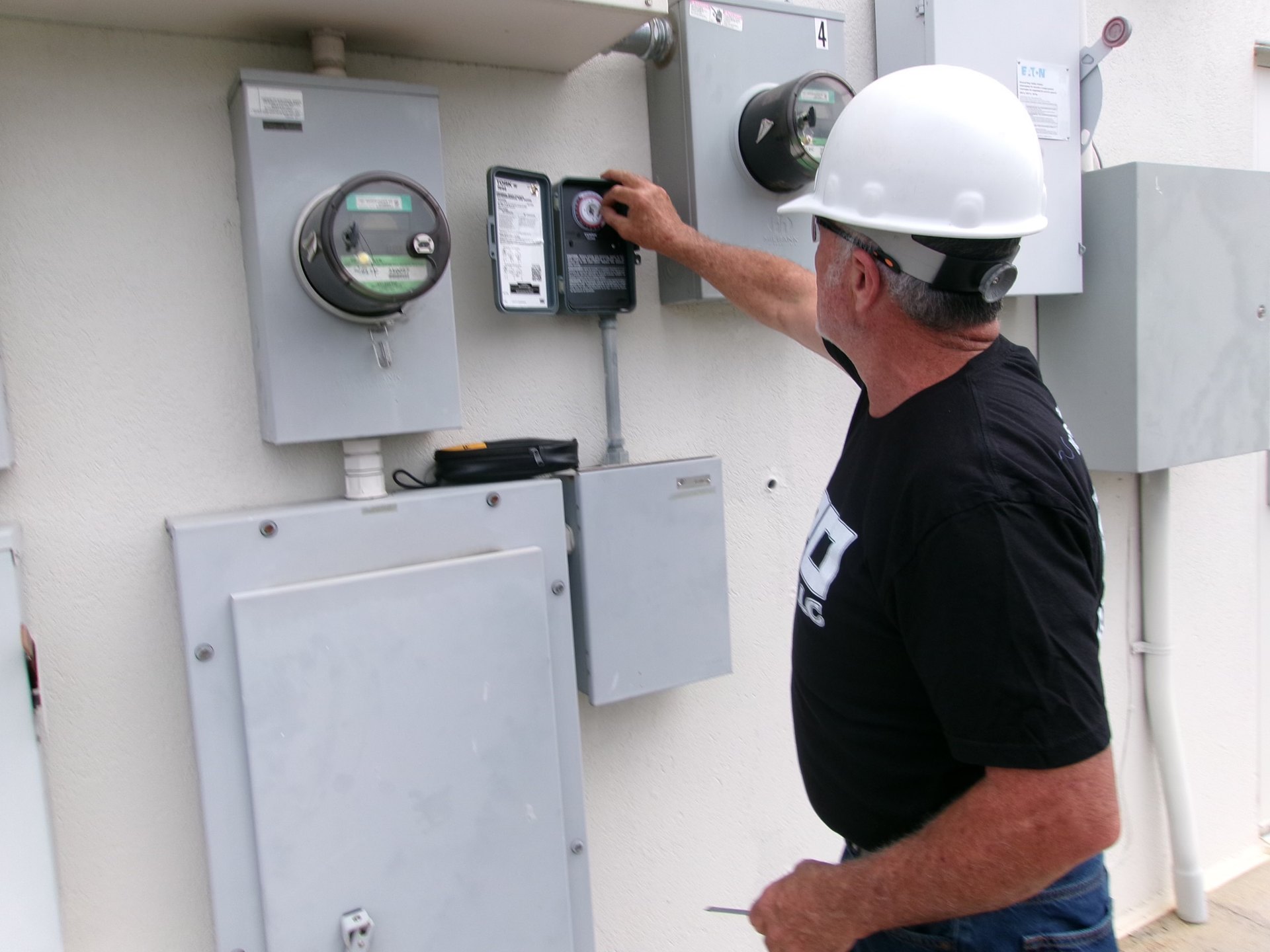 A man wearing a hard hat is working on an electrical box