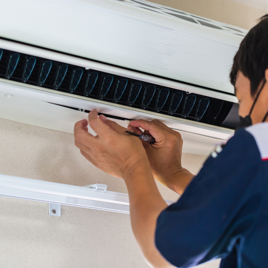 A man is fixing an air conditioner with a screwdriver
