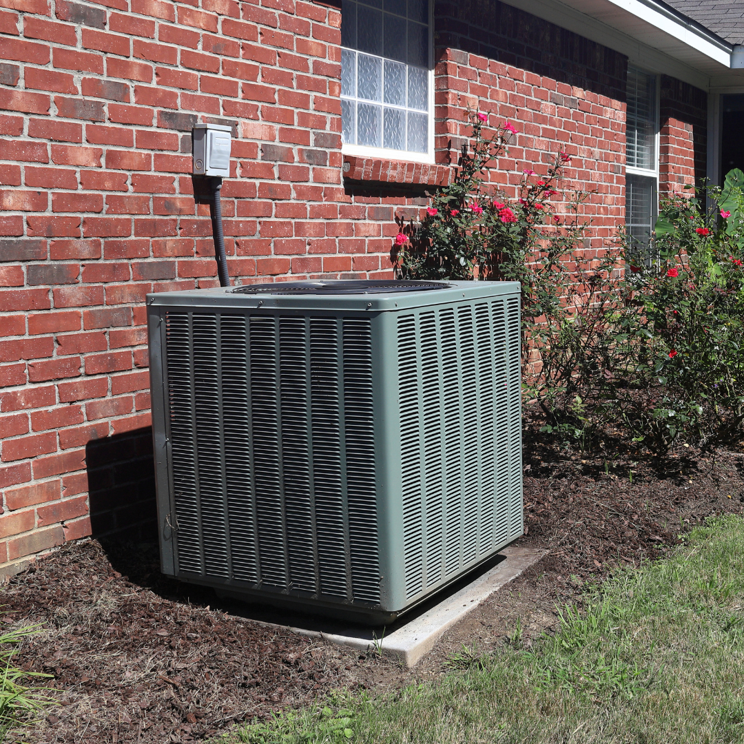 An air conditioner is sitting on the side of a brick house.