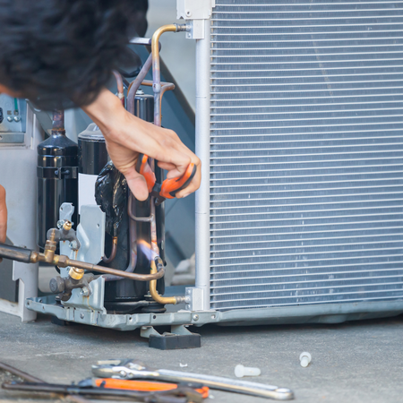 A technician uses a torch to solder copper pipes inside an air conditioning unit.