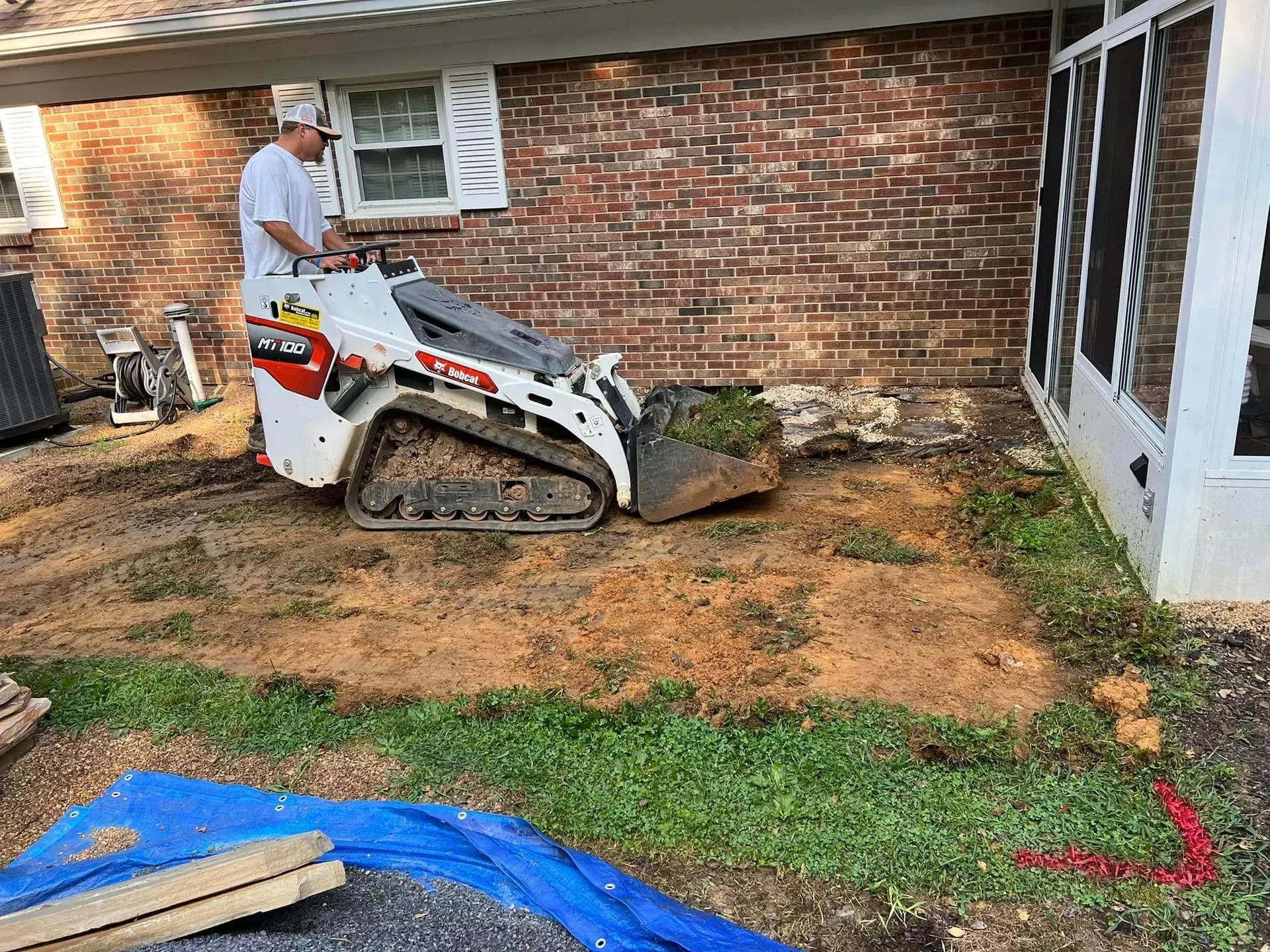 A man is driving a bulldozer in front of a brick house.