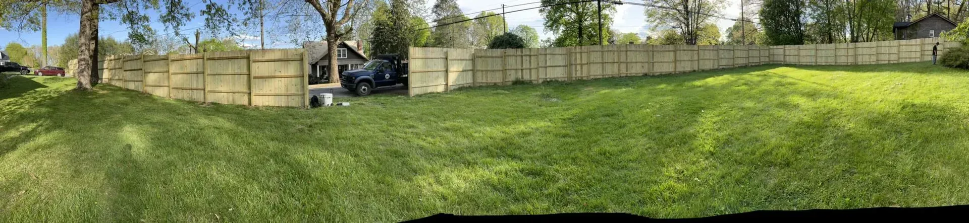 A panoramic view of a lush green yard with a wooden fence.