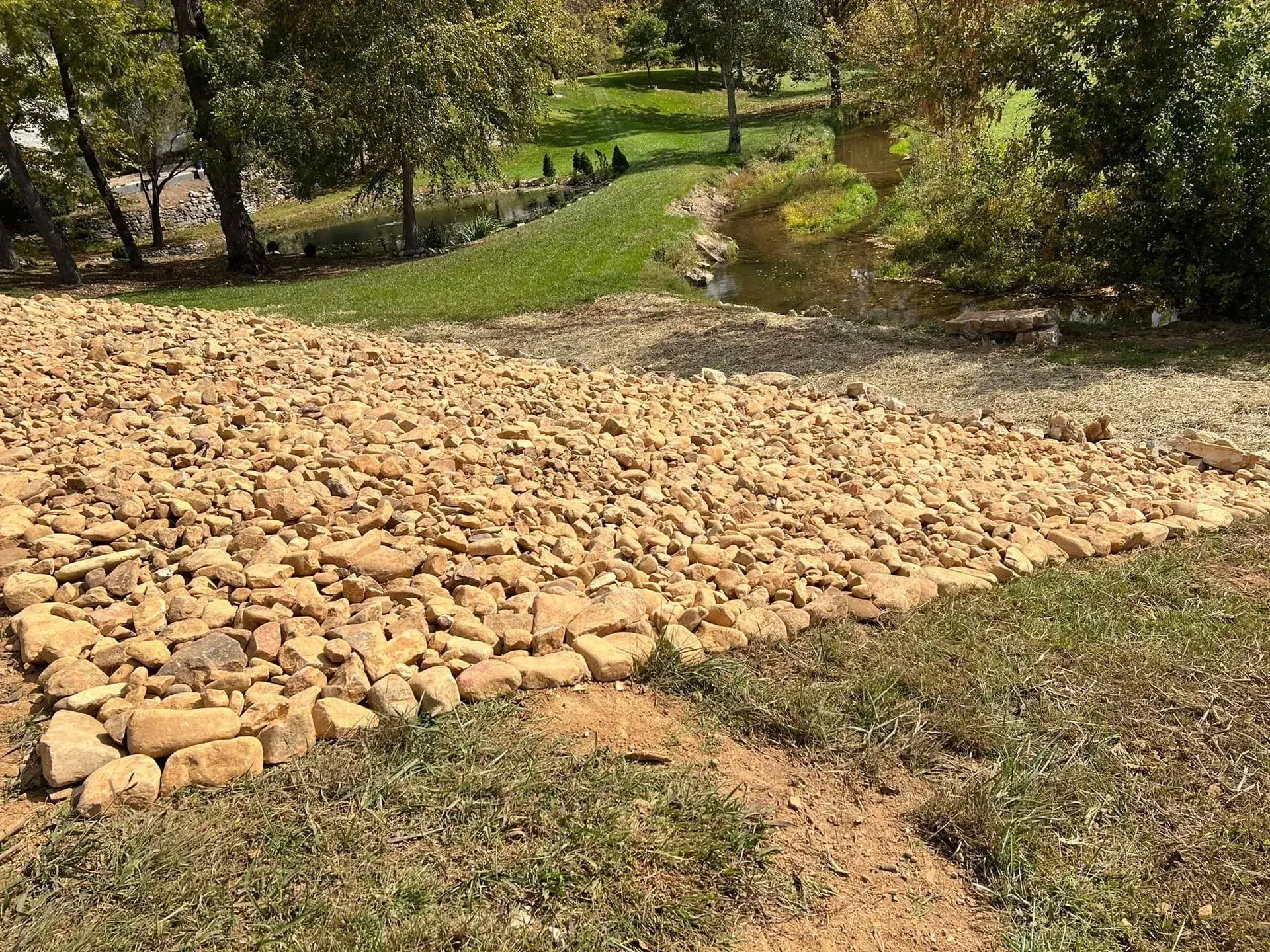 A pile of rocks sitting on top of a lush green field next to a river.