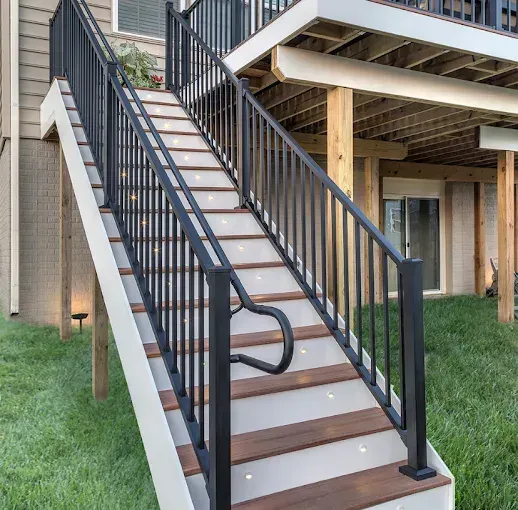 Outdoor staircase with black metal railing and built-in lighting on wooden steps, leading to a deck.