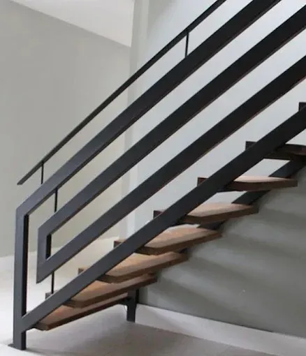 Staircase with wooden steps and black metal railing against a gray wall.