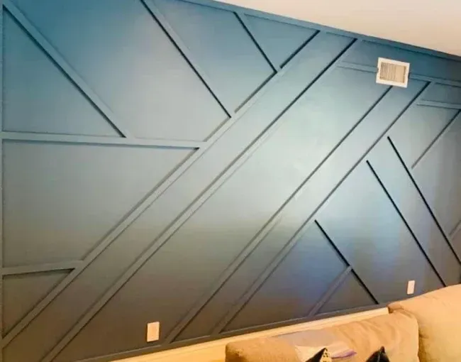 Blue geometric wall with built-in trim. Includes a vent, outlets, and part of a beige couch.