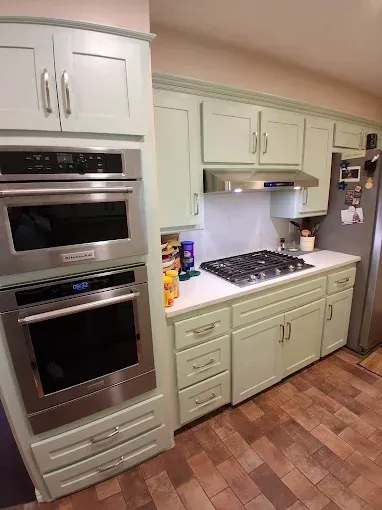 Mint green kitchen cabinets, stainless steel appliances, white countertop, gas cooktop.