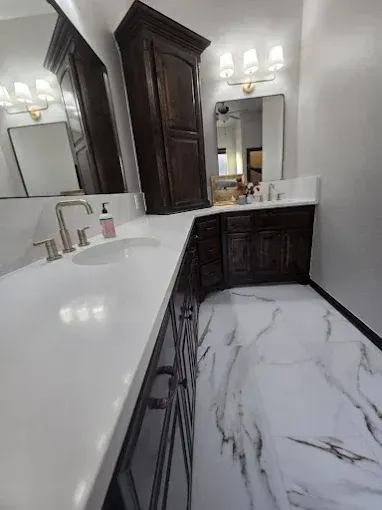 Bathroom with white countertops, dark wood cabinets, marble floors, and mirrors.