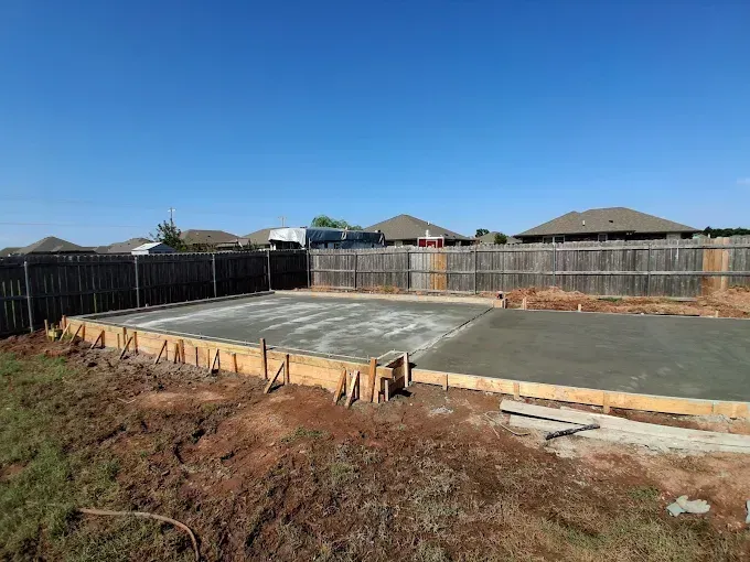 Newly poured concrete foundation in a backyard, surrounded by wooden framing and a fence.