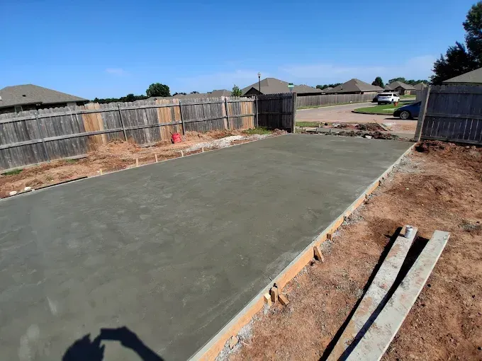 Freshly poured concrete patio in a backyard setting with a wooden fence.