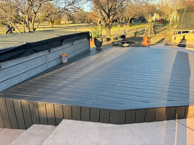 Large gray deck with surrounding fence, overlooking a yard with trees.