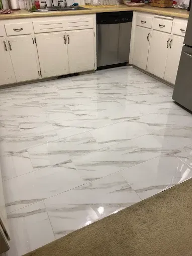 White marble-patterned flooring in a kitchen with white cabinets and a stainless steel dishwasher.