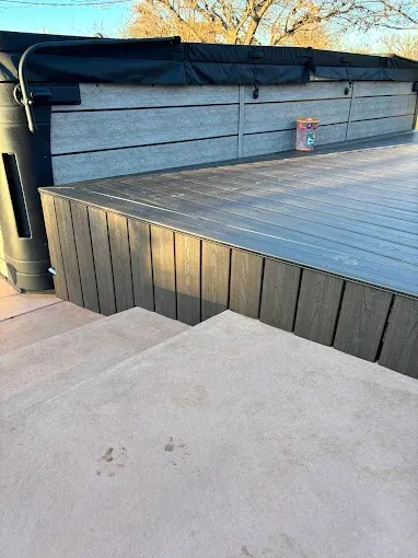 Concrete steps leading up to a deck with dark gray siding and a hot tub.