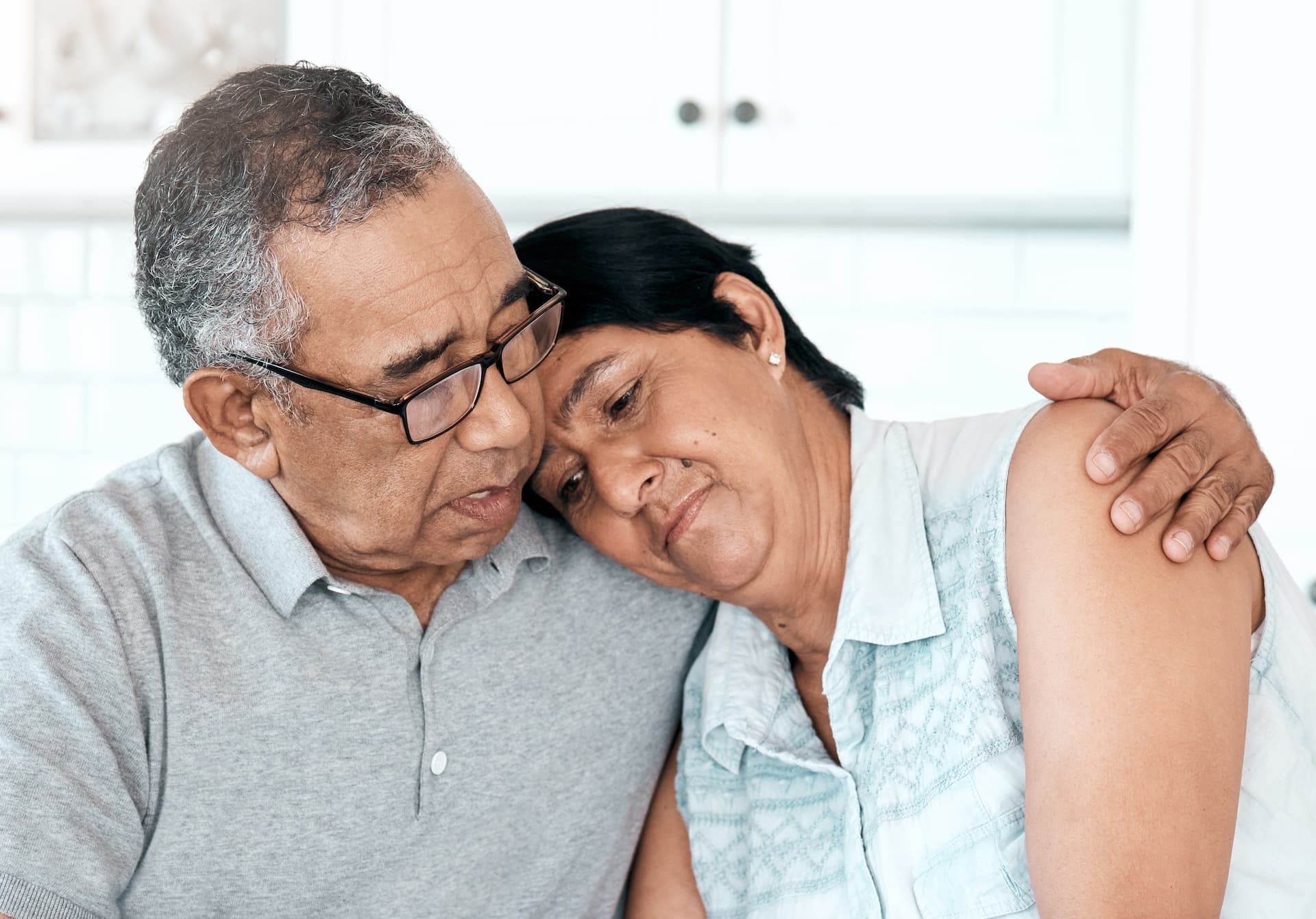 An elderly couple is hugging each other while sitting on a couch.