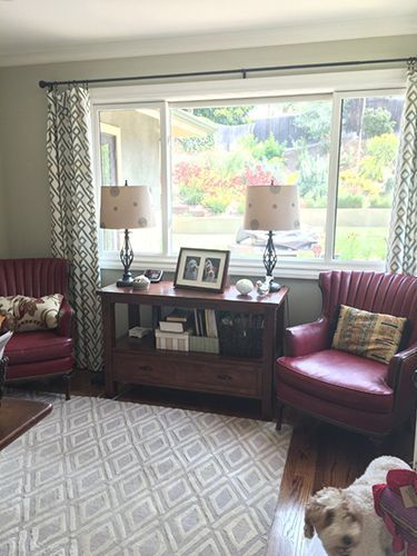 A living room with red chairs, a dog , a table and a window.