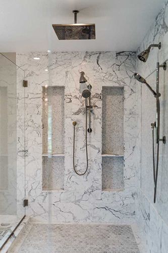 A bathroom with marble walls and a walk in shower with a ceiling mounted shower head.