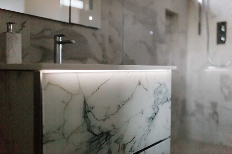 A bathroom with a marble counter top , sink , mirror and shower.