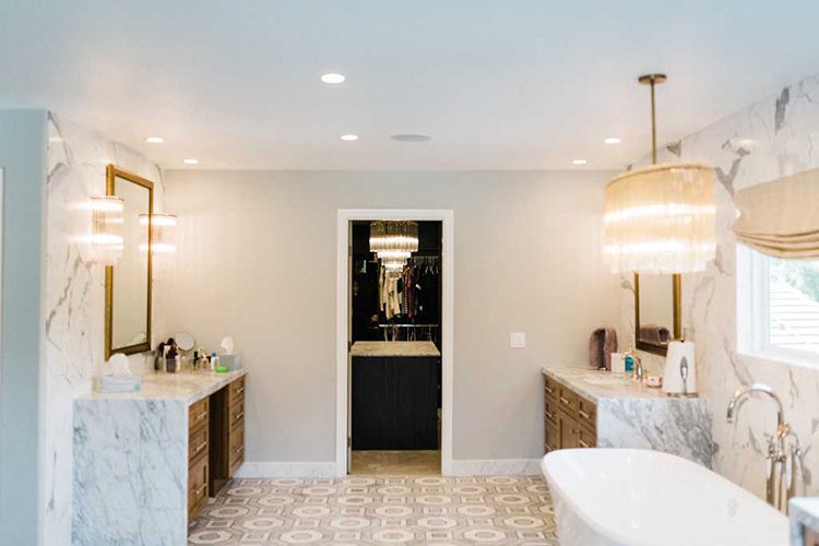 A bathroom with two sinks, a tub, a mirror and a chandelier.