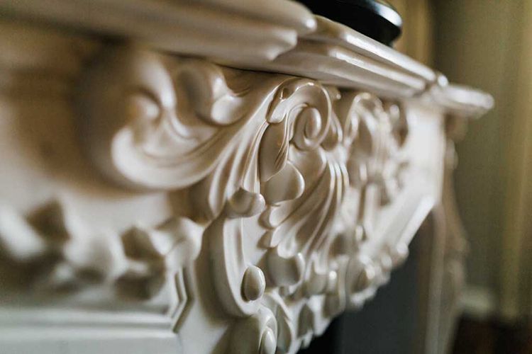 A close up of a white fireplace mantle with a carved design.