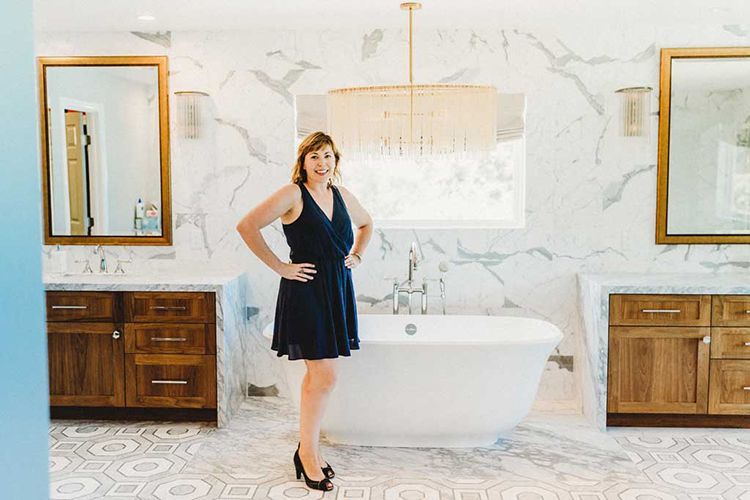 A woman in a blue dress is standing next to a bathtub in a bathroom.