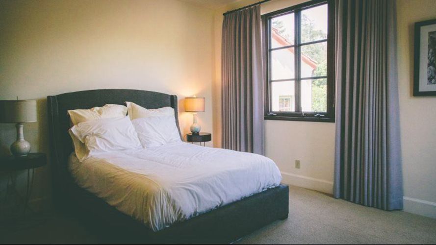 A bedroom with a bed , lamps , curtains and a window.