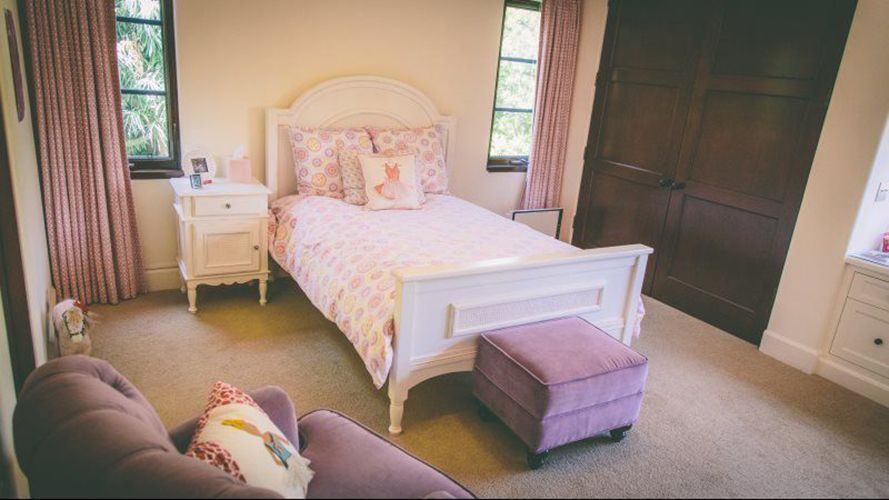 A bedroom with a bed , chair , nightstand and ottoman.