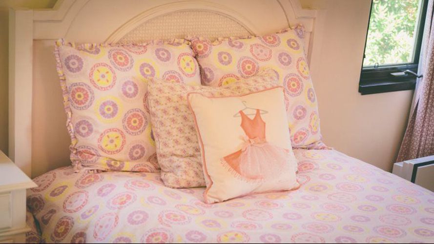 A bed with pink sheets and pillows and a pillow with a ballerina dress on it.