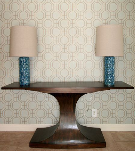 A table with two lamps on it in front of a wall with a pattern.