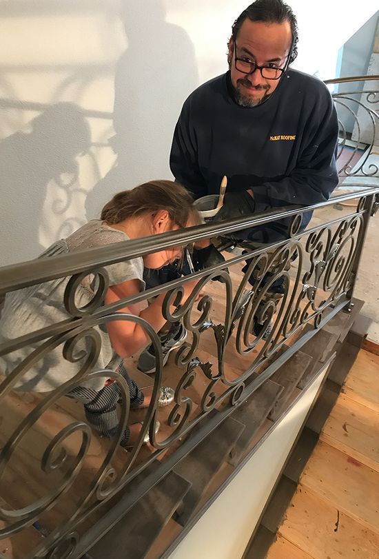 A man is working on a wrought iron railing on a staircase.