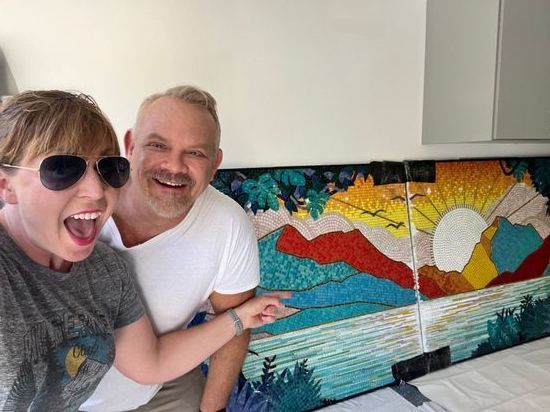 A man and a woman are posing for a picture in front of a painting.