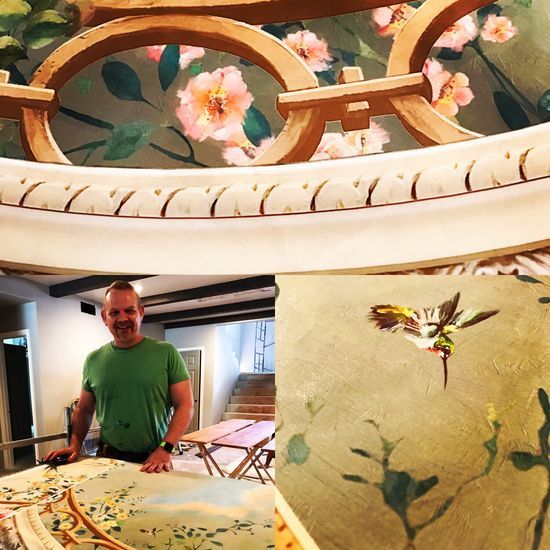 A man in a green shirt is standing in front of a painting of flowers