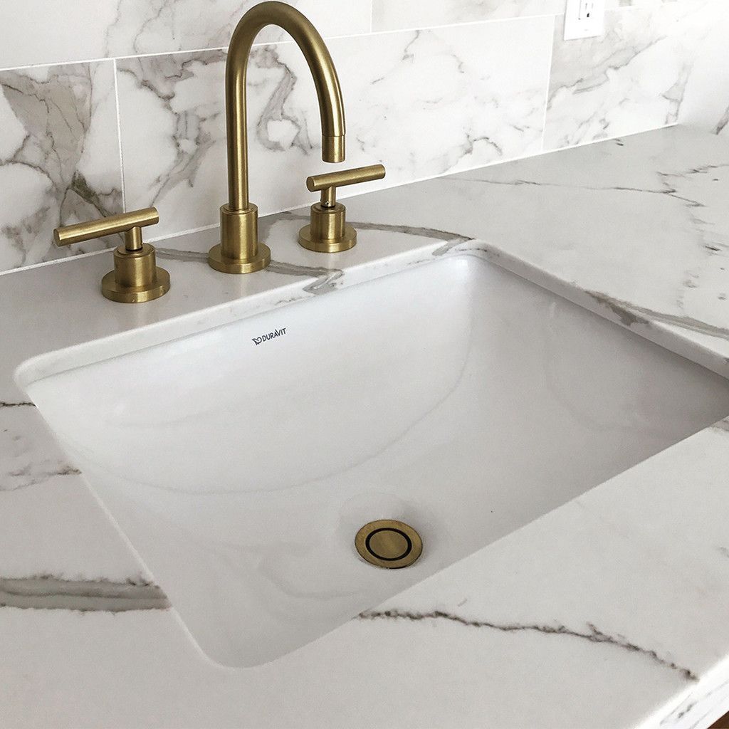 A bathroom sink with a brass faucet on a marble counter top.