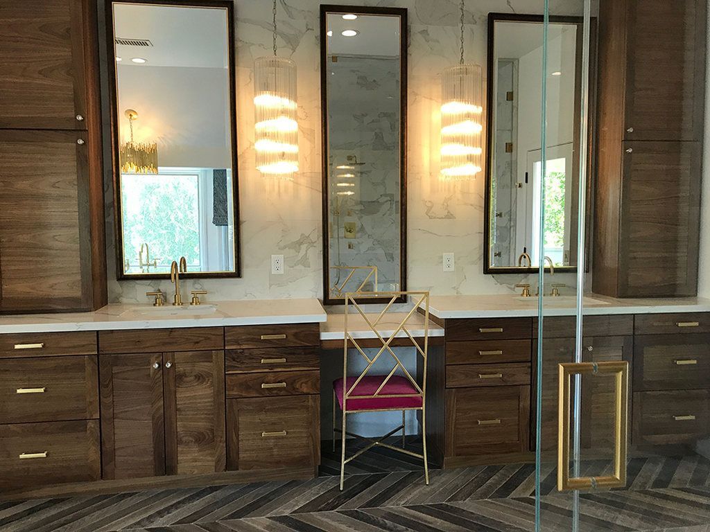A bathroom with two sinks , two mirrors and a chair.