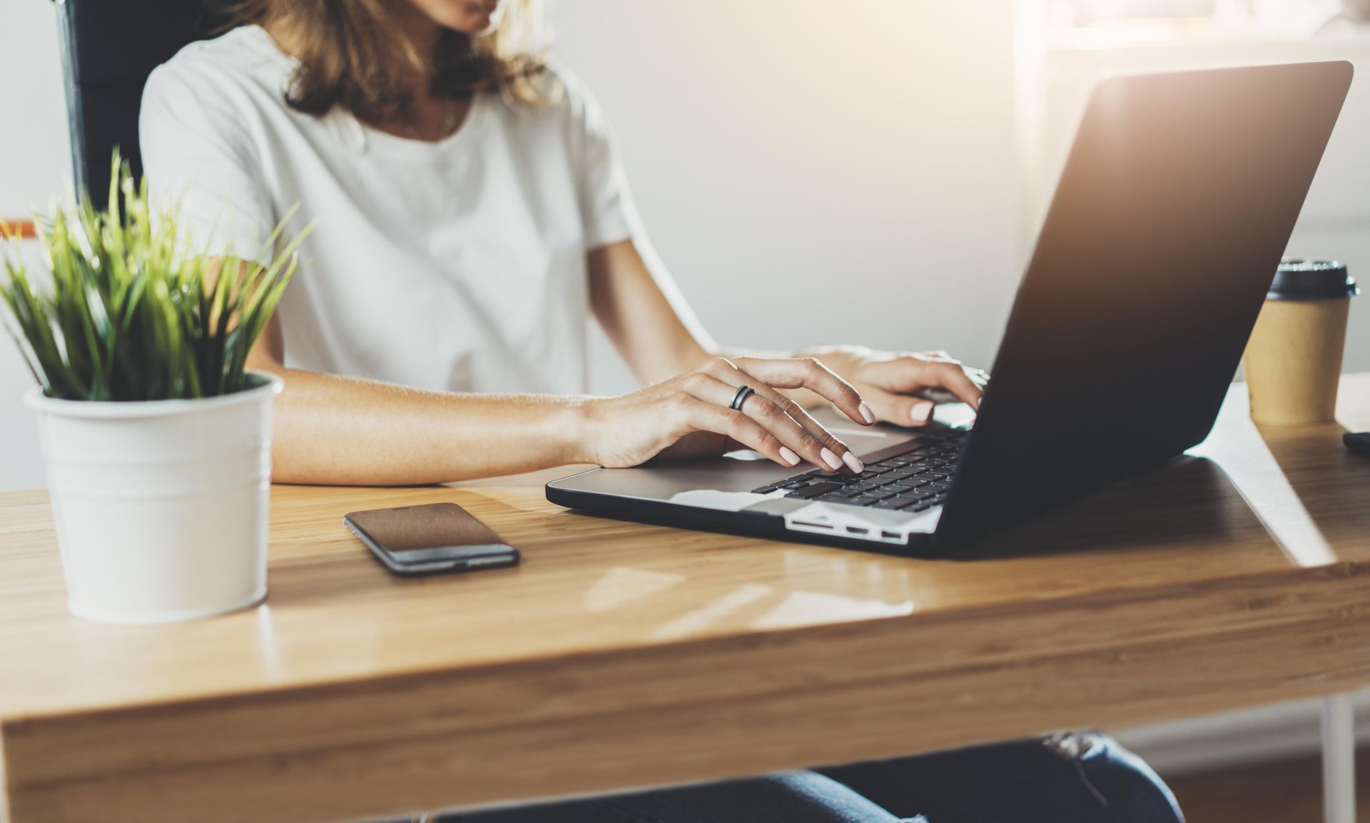 A woman is sitting at a desk typing on a laptop computer.