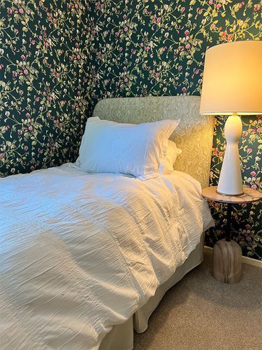 A bedroom with a bed, lamp, nightstand and floral wallpaper.