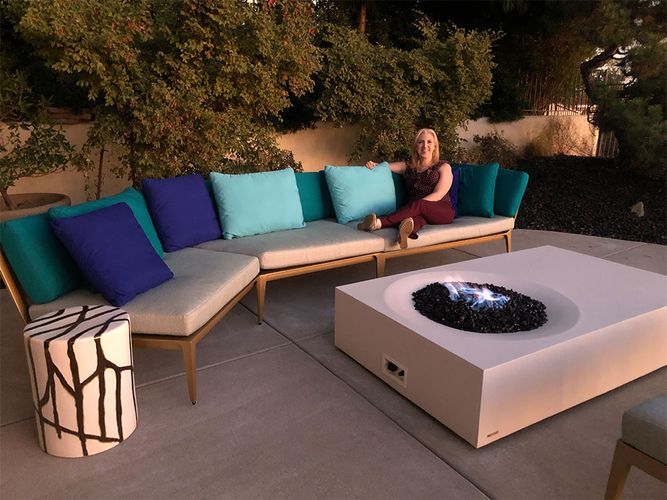 A woman is sitting on a couch next to a fire pit.