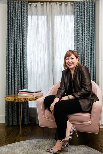 A woman is sitting in a pink chair in front of a window.