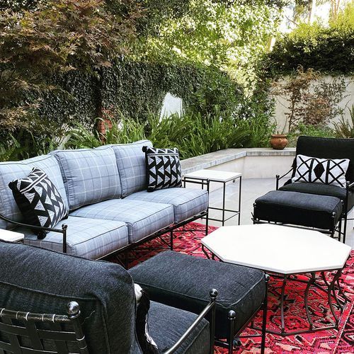 A patio with a couch , chairs , tables and a rug.